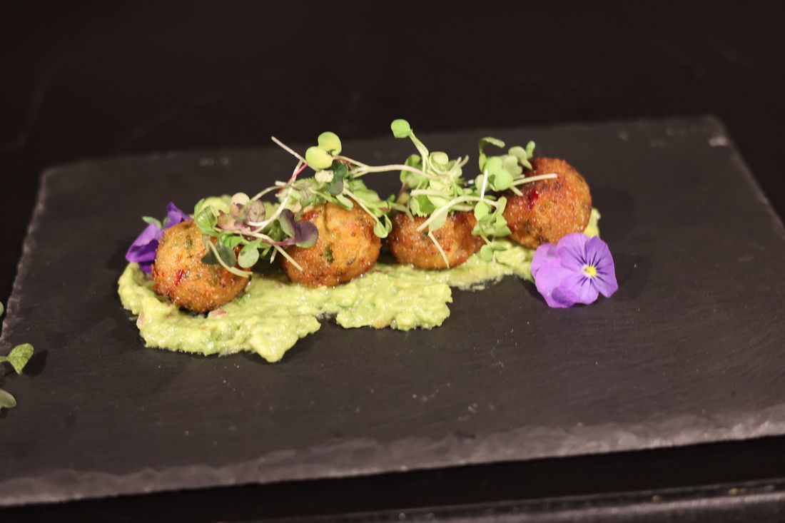 Four croquettes on slate over avocado purée, topped with microgreens.