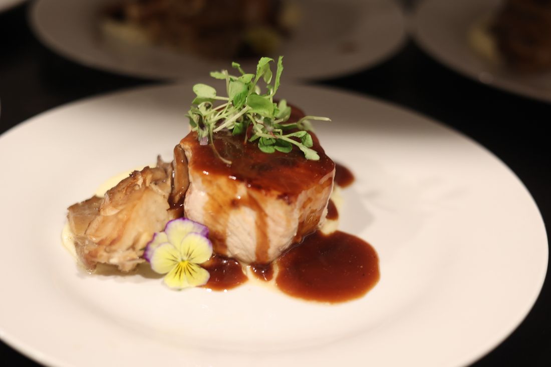 A seared pork chop over purée with demi-glace, microgreens and an edible pansy.